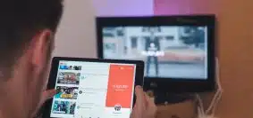 man browsing tablet sitting in front of TV